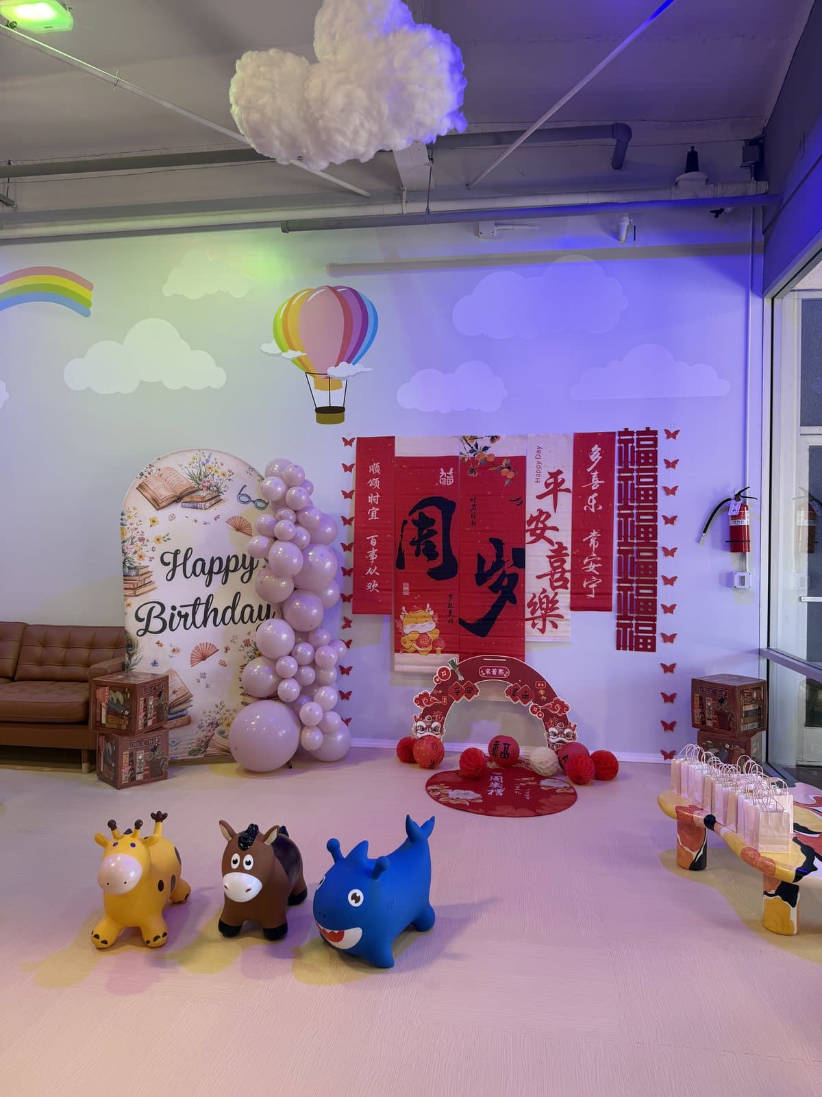 A birthday backdrop with balloons and a hot-air balloon, ride-on toys on the floor